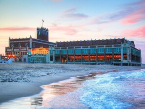A beachfront hotel with a prominent clock tower, a large building with multiple windows, and a beach in the foreground. - Perfect Neptune Getaway Minutes to Bradley Beach! (Neptune City)