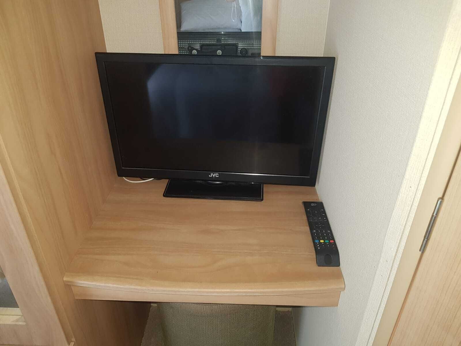 Een JVC televisie op een houten standaard, met een afstandsbediening ernaast.