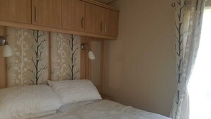 A bedroom with a bed, wooden cabinets, and two wall-mounted lamps. - Modern 6 berth caravan close to fishing lakes and beach (Burnham-on-Sea)