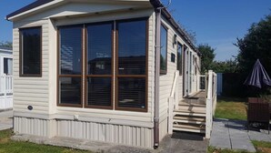 A single-story mobile home with large windows, a front porch, and a small deck. - Modern 6 berth caravan close to fishing lakes and beach (Burnham-on-Sea)