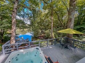 Un bain à remous sur une terrasse en bois, avec vue sur un lac, entouré d’arbres.
