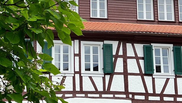 Ein traditionelles Fachwerkhäuschen mit rotem Ziegeldach, weißen Fensterrahmen und grünen Fensterläden.