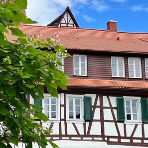 Uma casa tradicional em estilo de enxaimel, com telhado de telhas vermelhas, molduras de janelas brancas e venezianas verdes.