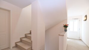 Eine Treppe mit beigen Stufen führt zu einer Zwischenebene, wo eine weiße Tür und ein Blumenvasen zu sehen sind.