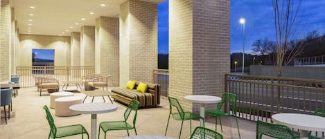 An outdoor patio area with round tables and green chairs, a sofa with yellow cushions, and brick walls.