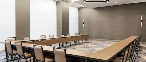 Un salón de conferencias con una larga mesa y sillas, iluminación moderna y suelo alfombrado.