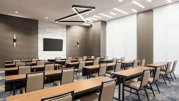 A conference room with multiple tables and chairs, a large screen, and a modern ceiling light fixture.