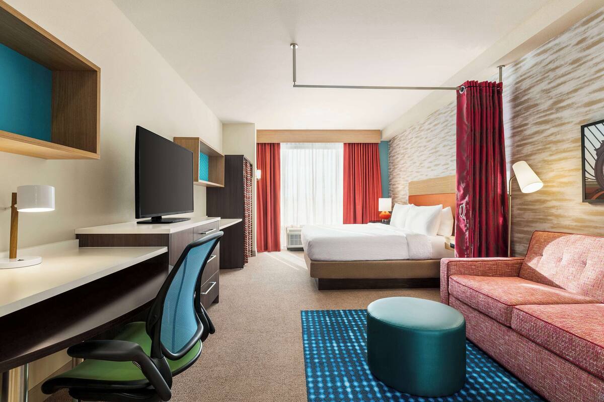 A hotel room with a bed, a desk with a computer, a chair, a sofa, and a TV.