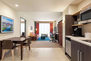 Ein modernes Hotelzimmer mit Essbereich, einer Küchenzeile und einem großen Fenster mit Vorhängen.