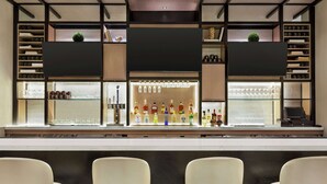 Un espace bar comprenant un comptoir, des étagères remplies de bouteilles et trois tabourets de bar.