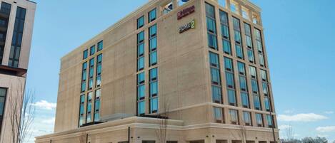 Un moderno edificio de hotel con un llamativo letrero de "Hilton Garden Inn", varios pisos y un amplio área de entrada.