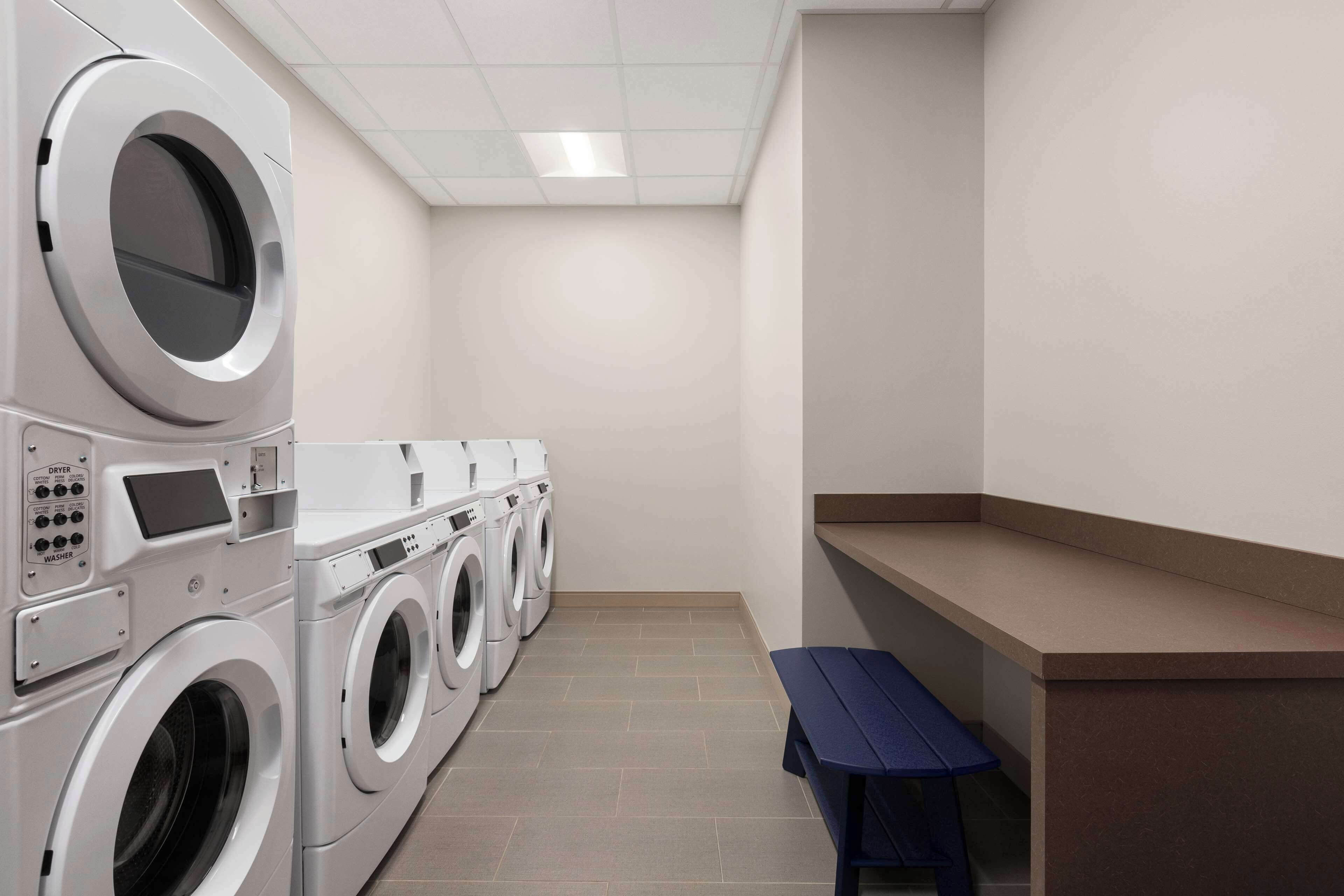 A laundry room with multiple washing machines, a bench, and a control panel.