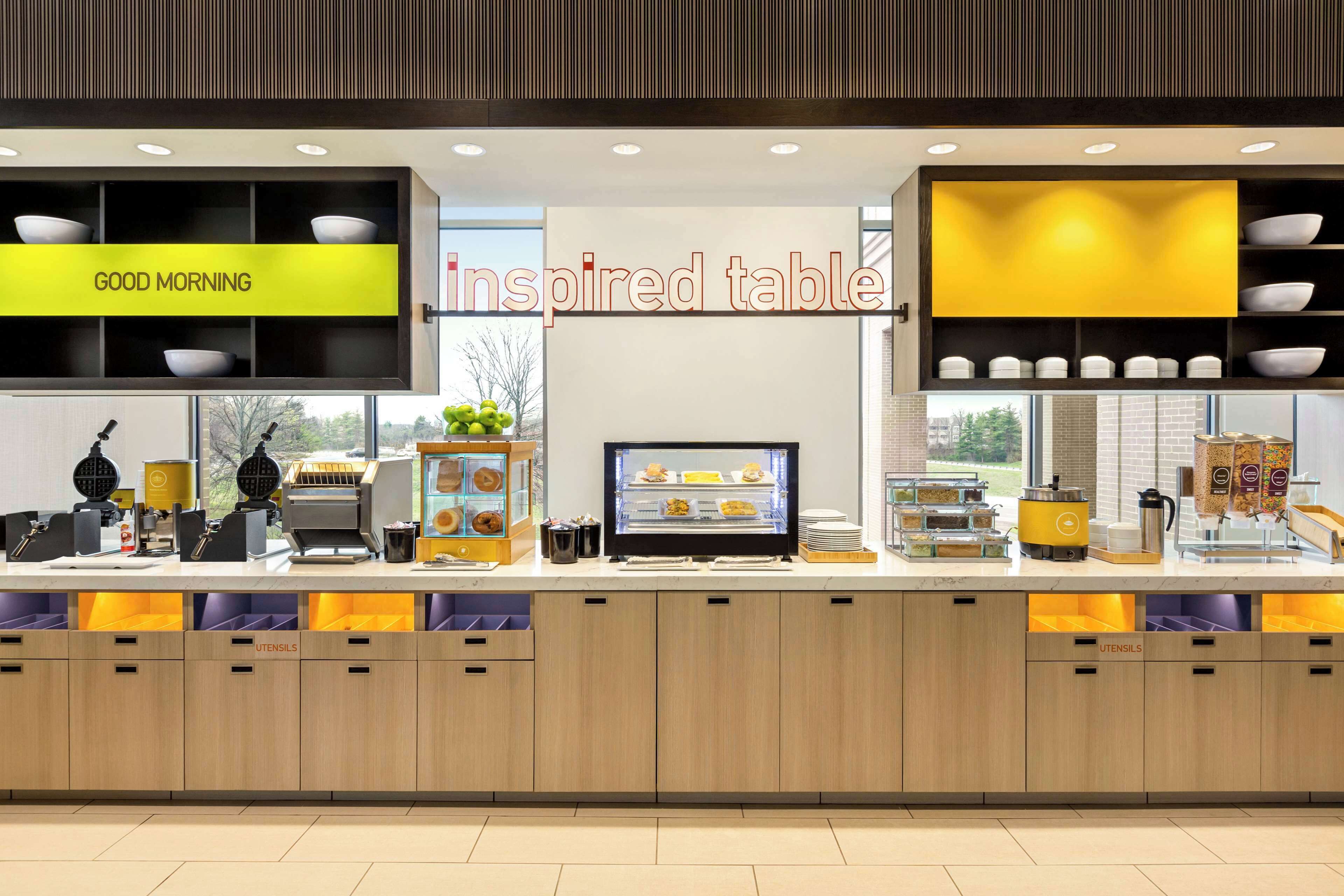 A breakfast bar with a 'Good Morning' sign, a display case with pastries, and a 'Inspired Table' sign.