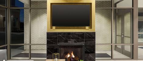 Una sala de estar moderna con chimenea, un televisor de pantalla plana montado encima y un gran ventanal que da a un área exterior.