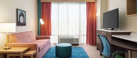 Habitación de hotel con sofá, reposapiés, escritorio, silla, televisor y aire acondicionado.