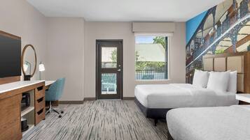 A hotel room with two beds, a desk with a chair, a large mirror, and a view of a bridge through the window.