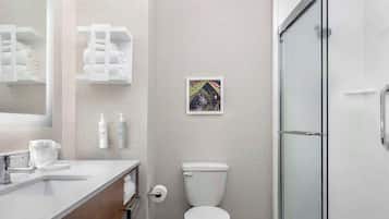 A modern bathroom with a toilet, sink, and shower. There are towels and toiletries on the counter.