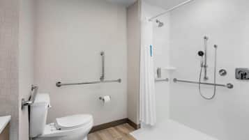 A bathroom with a toilet, a shower with grab bars, and a white tiled wall.