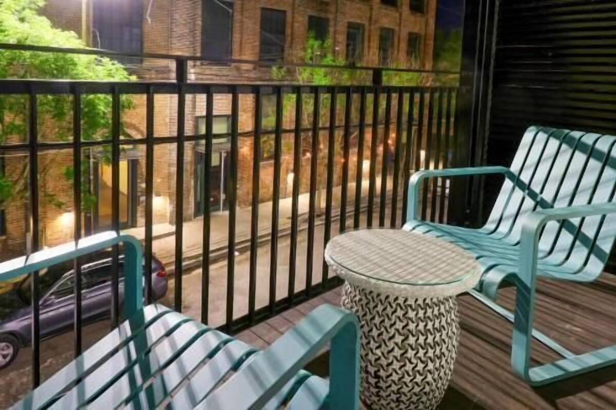 A balcony with metal railings, two green chairs, a small round table, and a parked car.