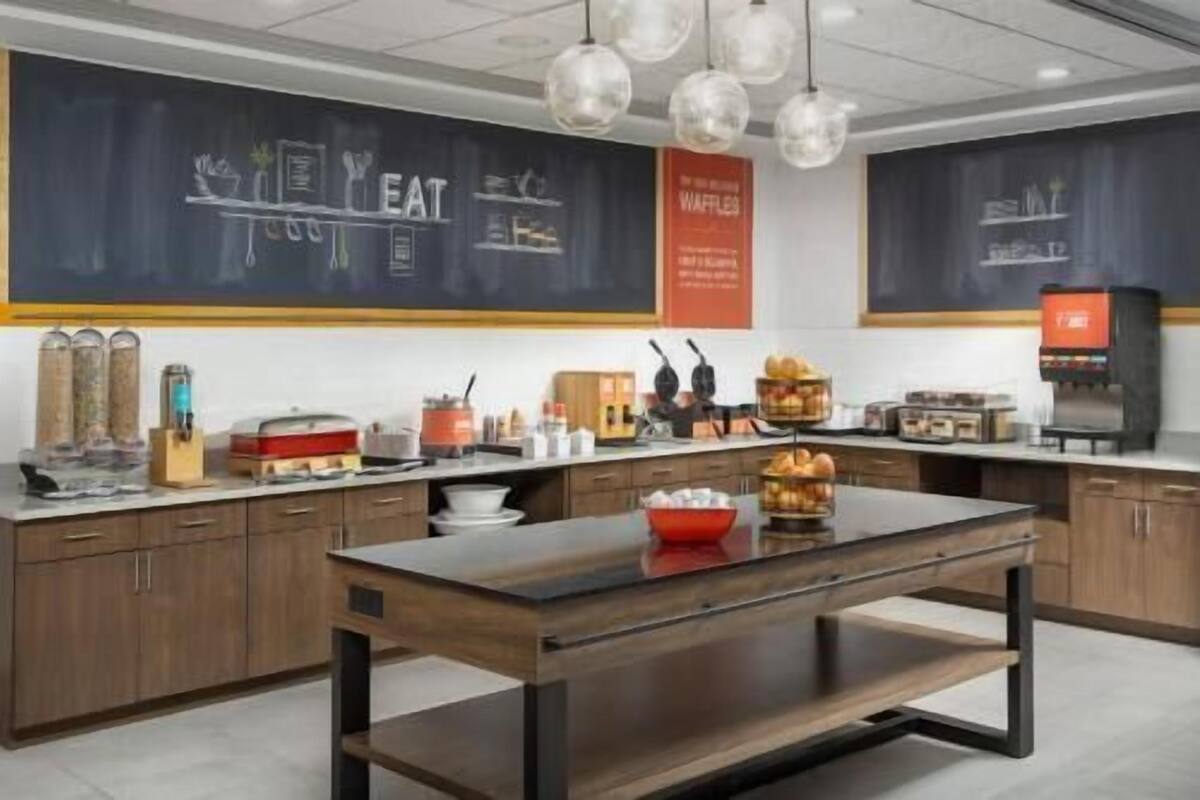 A modern kitchen with a central island, a chalkboard with writing, and various kitchen appliances.