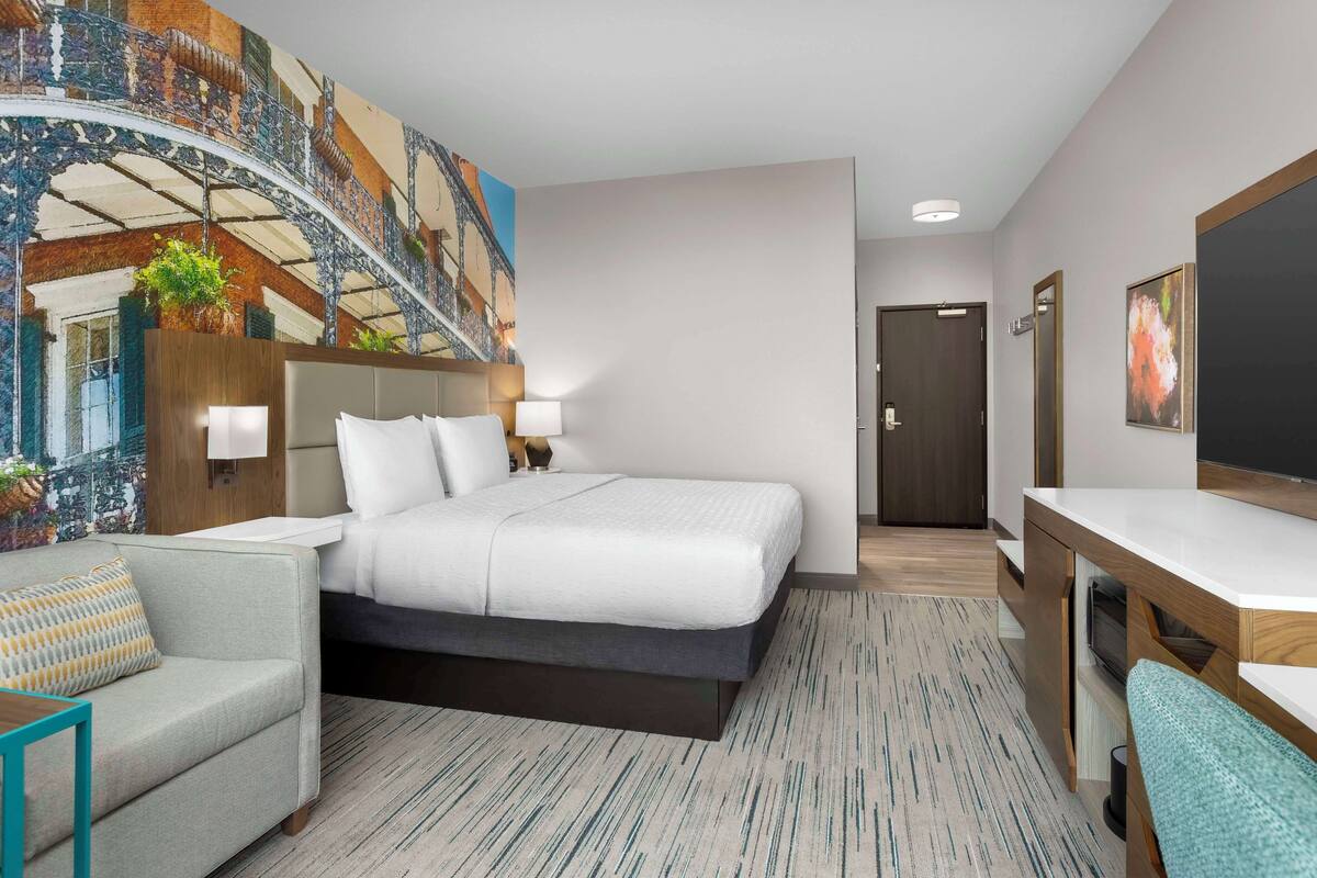 A hotel room with a bed, a desk, a chair, a large mural, and a staircase.