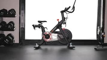 An exercise bike in a room with a wall-mounted dumbbell rack and a door leading to another room.
