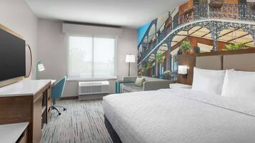 A hotel room with a large bed, a desk, a chair, a window with blinds, a wall mural, and a ceiling fan.