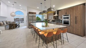 Een moderne keuken met een centraal eiland, houten kastjes, roestvrijstalen apparatuur en een eethoek met uitzicht.