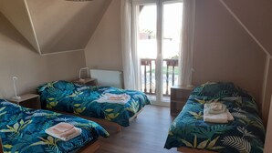 Ein Zimmer mit zwei Betten, jeweils mit Bettwäsche mit Blättermotiv, einem Nachttisch mit Lampe und Blick ins Freie durch eine Glastür.