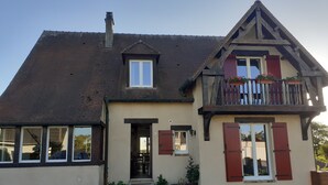 Ein zweistöckiges Haus mit einem steilen Satteldach, einem Balkon mit roten Fensterläden und einer kleinen Veranda.