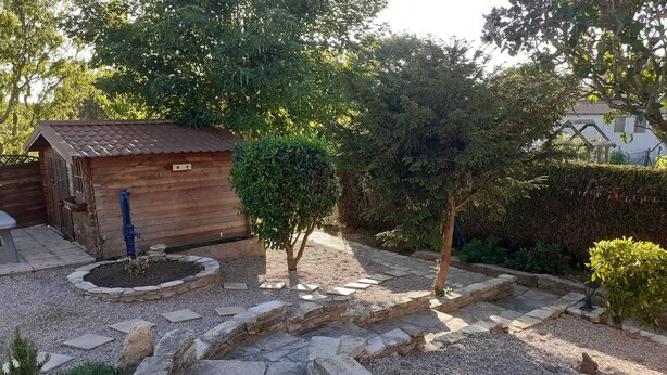 Eine Holzhütte mit einem Metalldach, umgeben von einem Kiesweg und Steinstufen, die zu einer Holzterrasse führen.