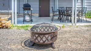 Un foyer extérieur aménagé dans un espace recouvert de gravier, avec un barbecue et des chaises, situé devant un bâtiment.
