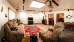 Un salon avec un canapé, un tapis, un ventilateur de plafond et un téléviseur.