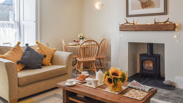 Una sala de estar acogedora con un sofá, una mesa de comedor con sillas, una chimenea y un cuadro en la pared.