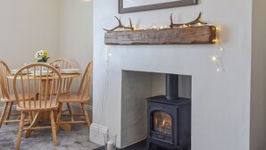 Un comedor acogedor con una mesa y sillas de madera, una chimenea con estufa moderna, y una estantería decorativa con cornamentas e iluminación.