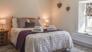 Una cama bien hecha con una colcha blanca y morada, dos lámparas de noche y una ventana con vistas.