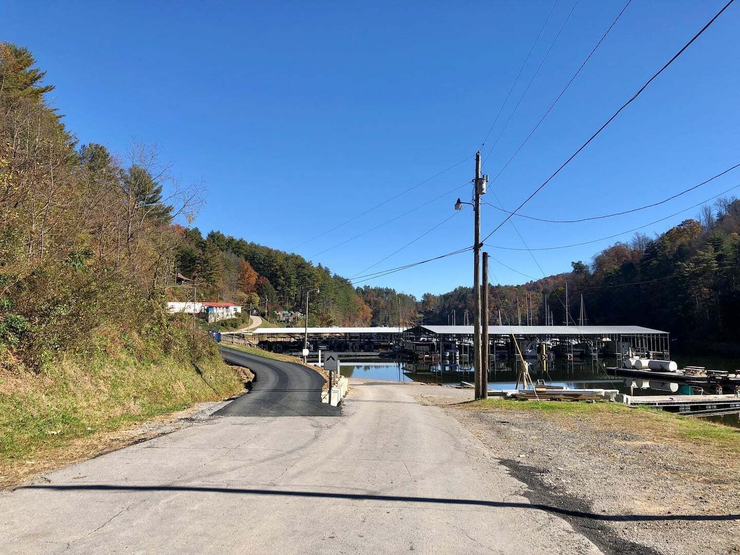 A rural road leading to a dock area with boats, surrounded by trees and a clear sky.