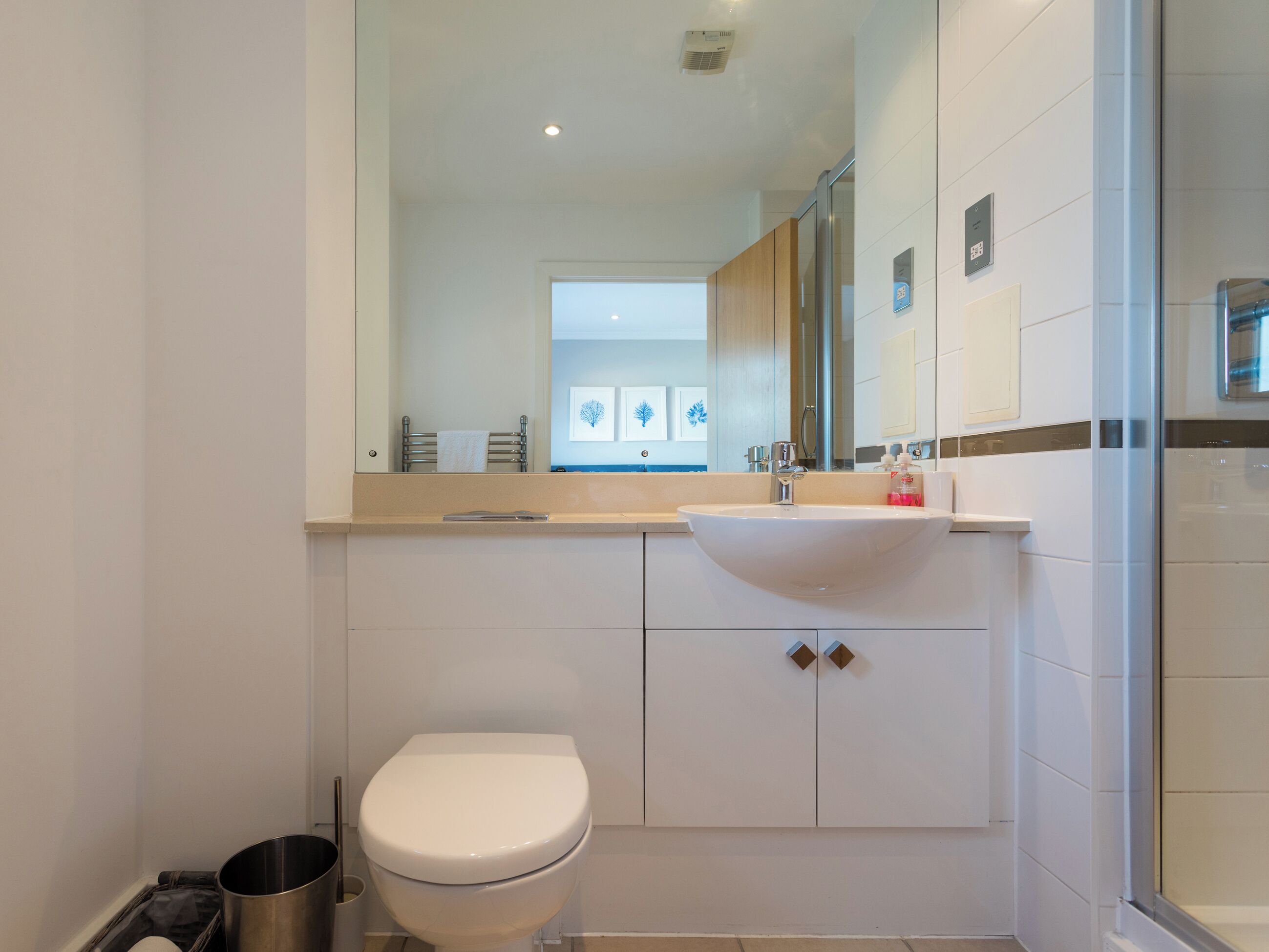 Un baño moderno con inodoro blanco, lavabo con espejo y zona de ducha.