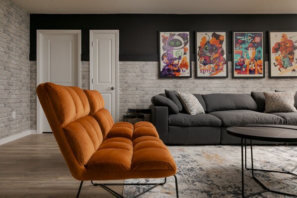 A modern living room with a brick wall, a grey sofa, an orange armchair, and a coffee table.
