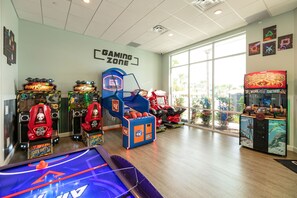 Una zona de juegos con diversas máquinas recreativas, una mesa de billar y un amplio ventanal con vistas al exterior.