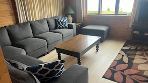 Een gezellige woonkamer met een grijze bank, een houten salontafel en een kamerbreed tapijt.