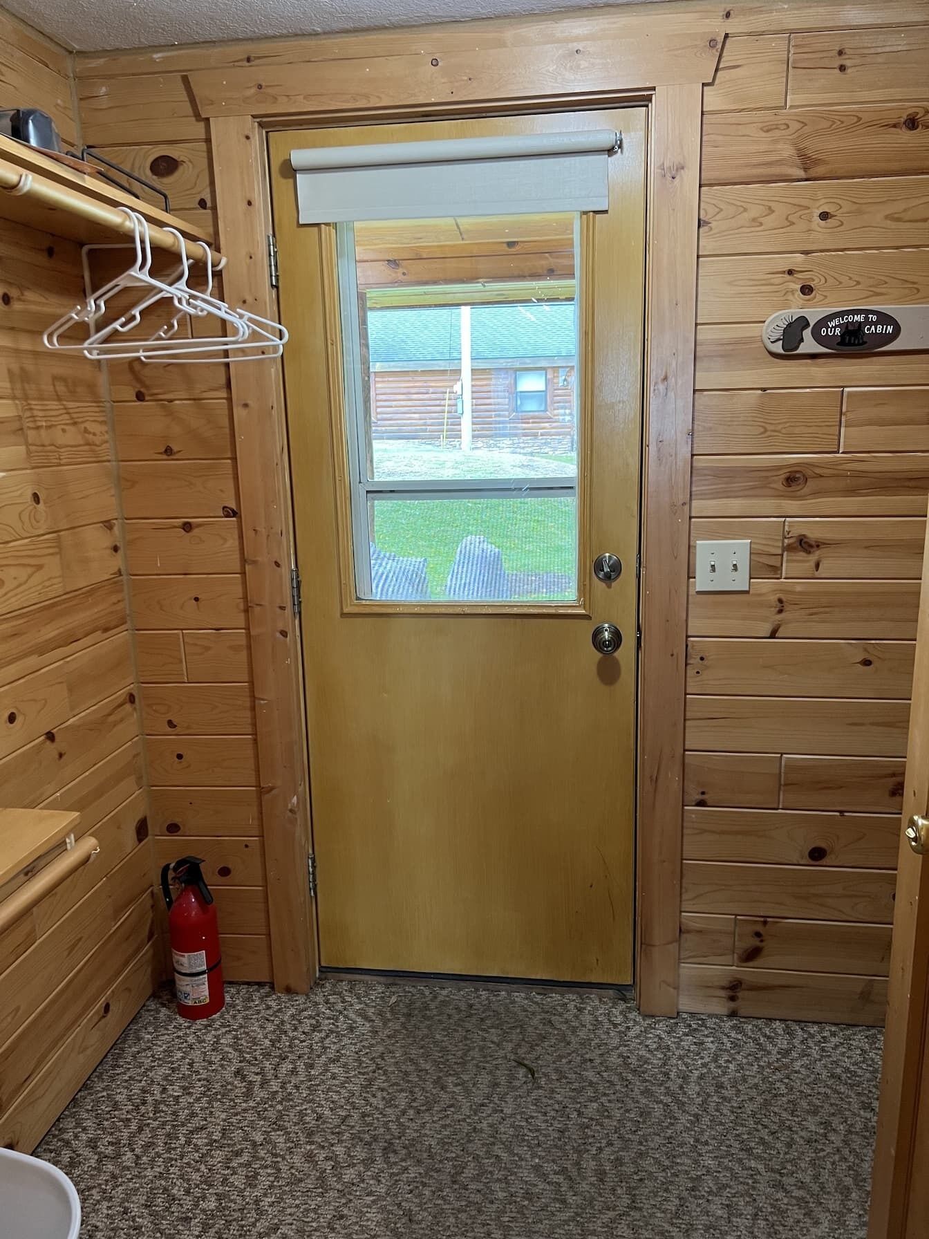 A wooden cabin interior with a door, a fire extinguisher, and a welcome sign.
