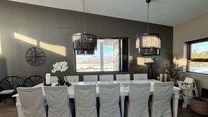 Comedor con una mesa larga, sillas blancas y dos lámparas colgantes.
