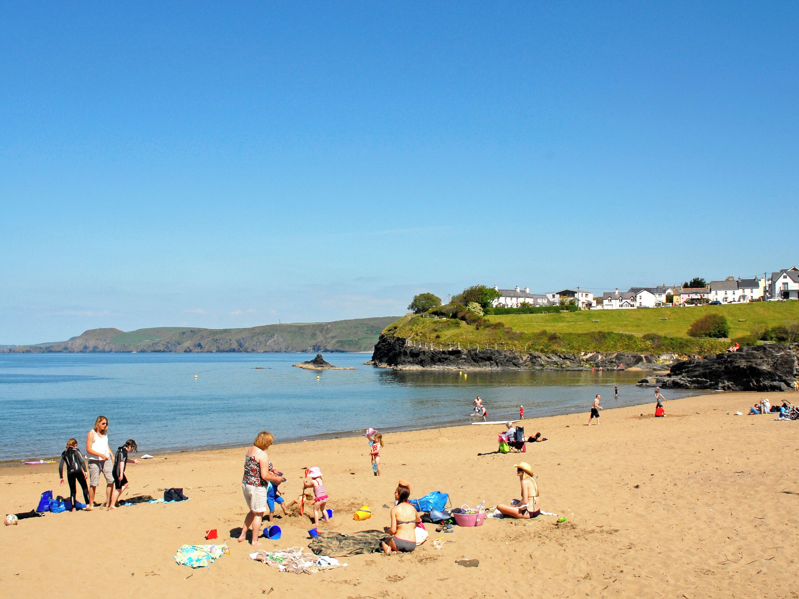 A beach with people, a clear sky, and houses in the background.