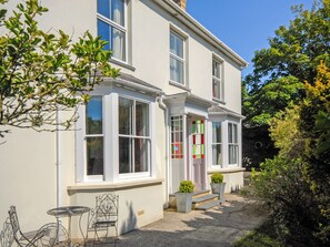 A two-story house with a front porch, a small outdoor seating area with a table and chairs, and a pathway leading to the entrance. - 5 bedroom accommodation in Tresaith, near Aberporth (Tresaith, near Aberporth)