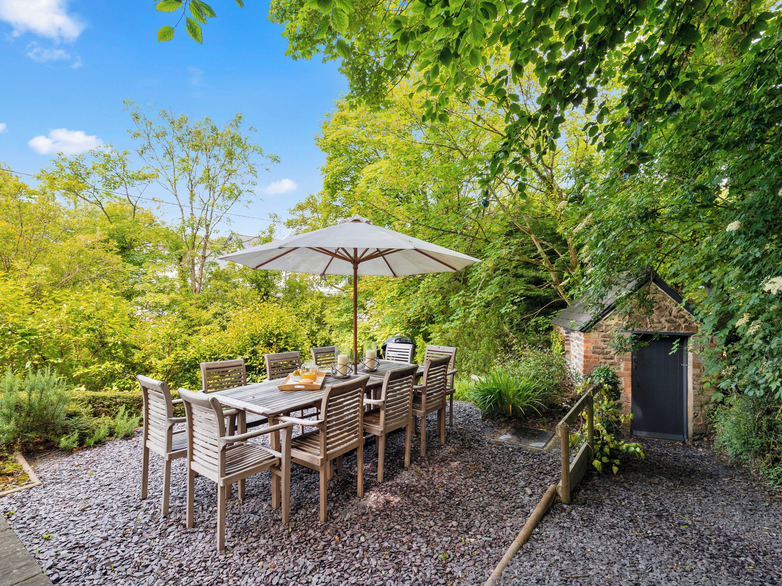 An outdoor dining area with a table and chairs, surrounded by gravel and greenery.