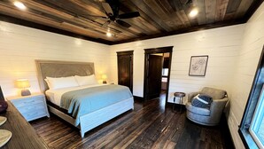 Un dormitorio con cama, mesitas de noche, una silla, ventilador de techo y ventana.