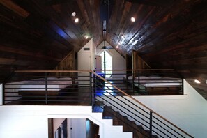 Ein Schlafzimmer im Loft-Stil mit einer zentralen Treppe, Holzbalken und einem Oberlicht.
