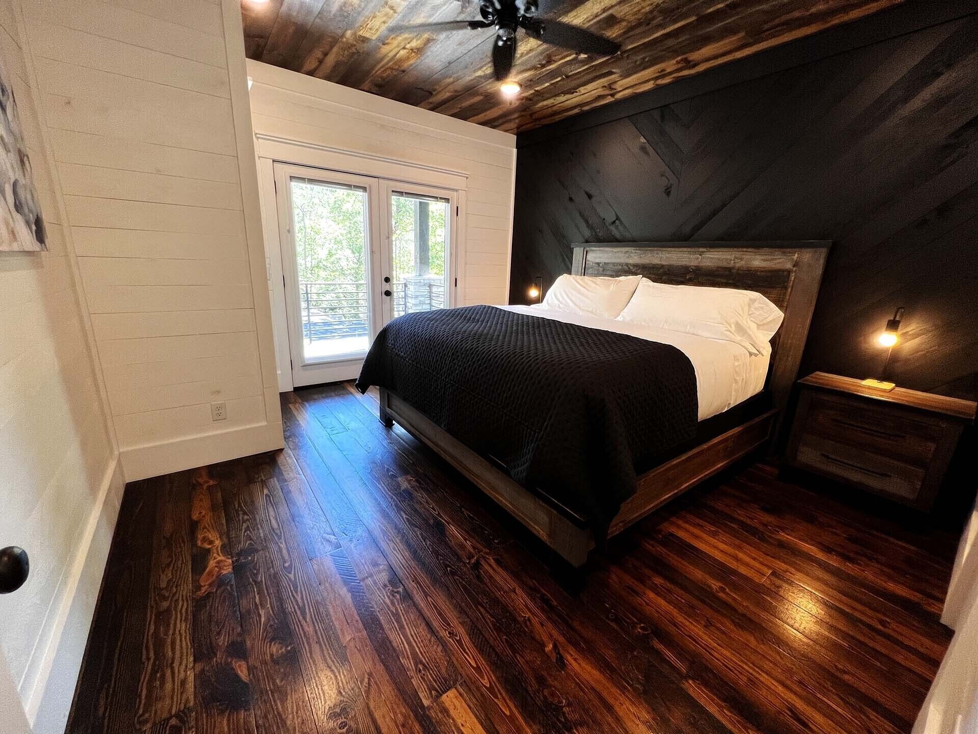 Ein Schlafzimmer mit einem Holzbett, einem Nachttisch, einem Deckenventilator und Blick ins Freie durch eine Schiebetür.