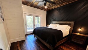 A bedroom with a wooden bed, a nightstand, a ceiling fan, and a view of the outdoors through a sliding door. - Lakeside | Hot Tub | Kayaks | Fishing (MENA)
